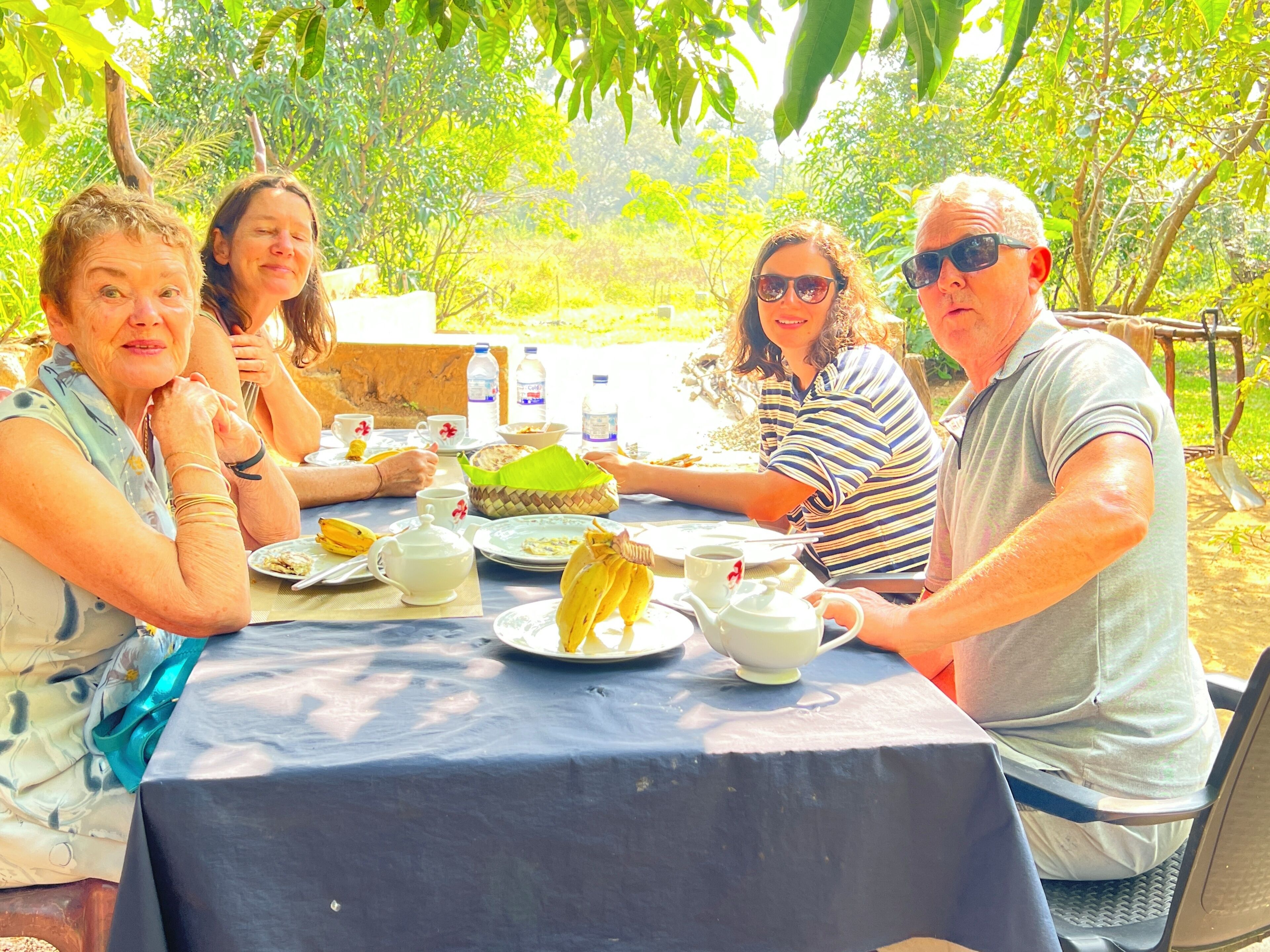A group of people dining outdoors at a table with a blue tablecloth, surrounded by greenery.