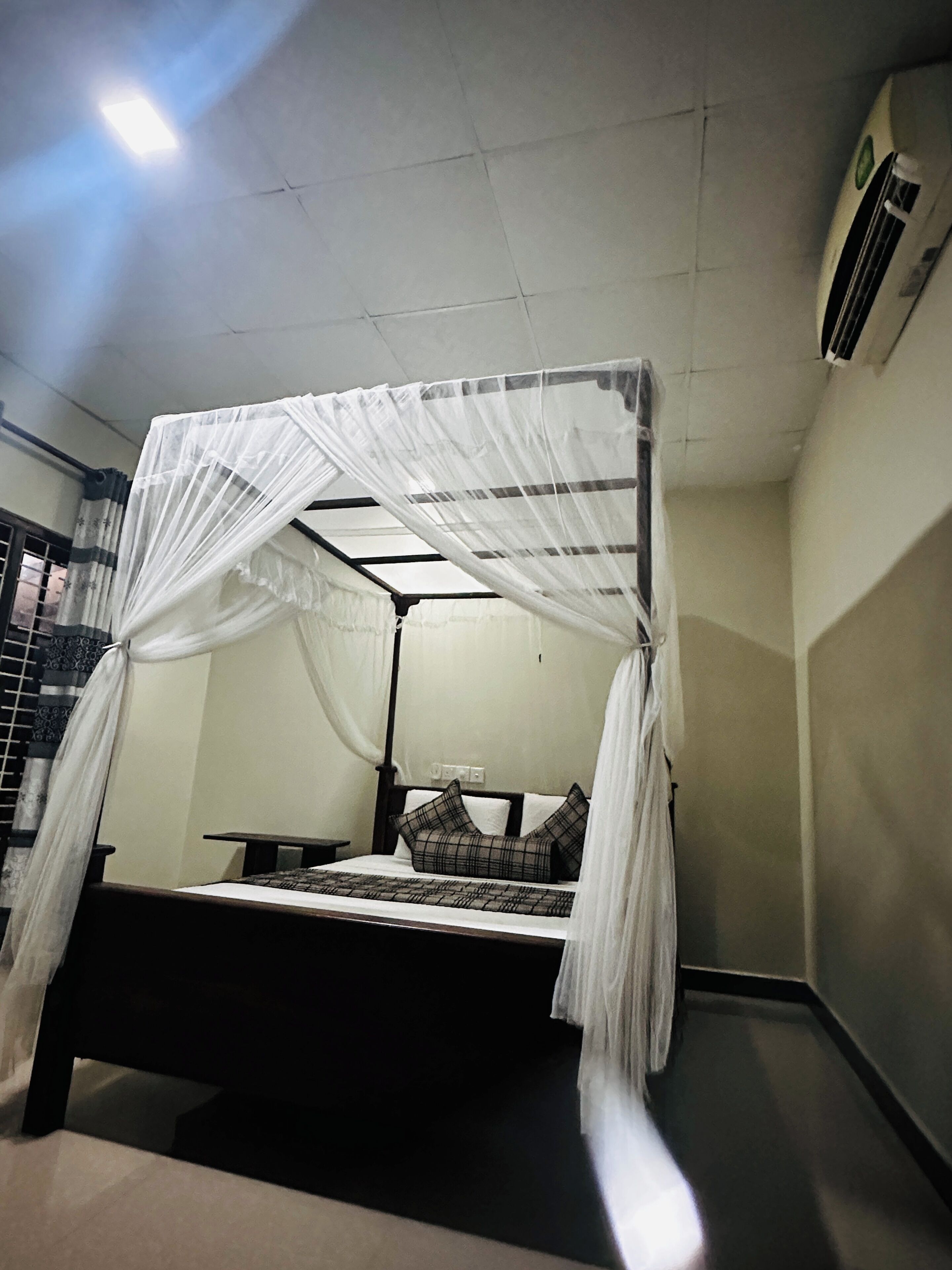 A bed with a canopy, a bedside table, and a wall-mounted air conditioning unit.