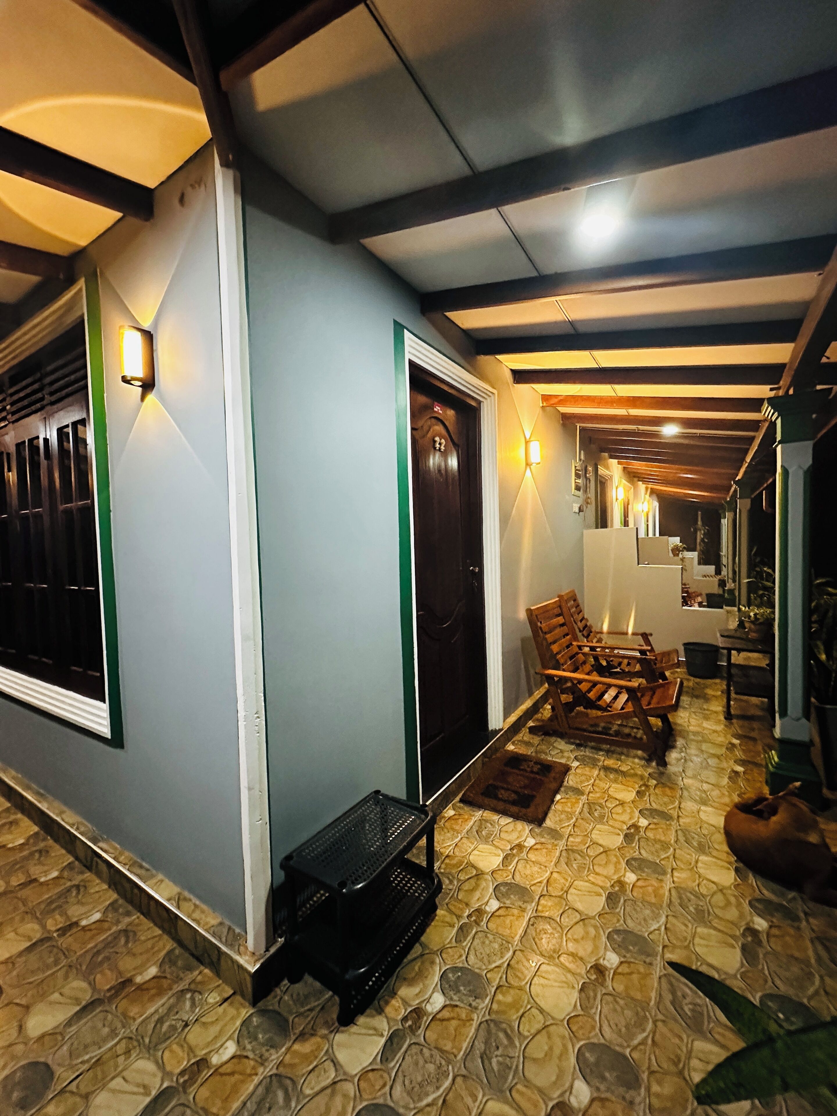 A hallway with a stone-tiled floor, a wooden door, and a seating area with chairs.