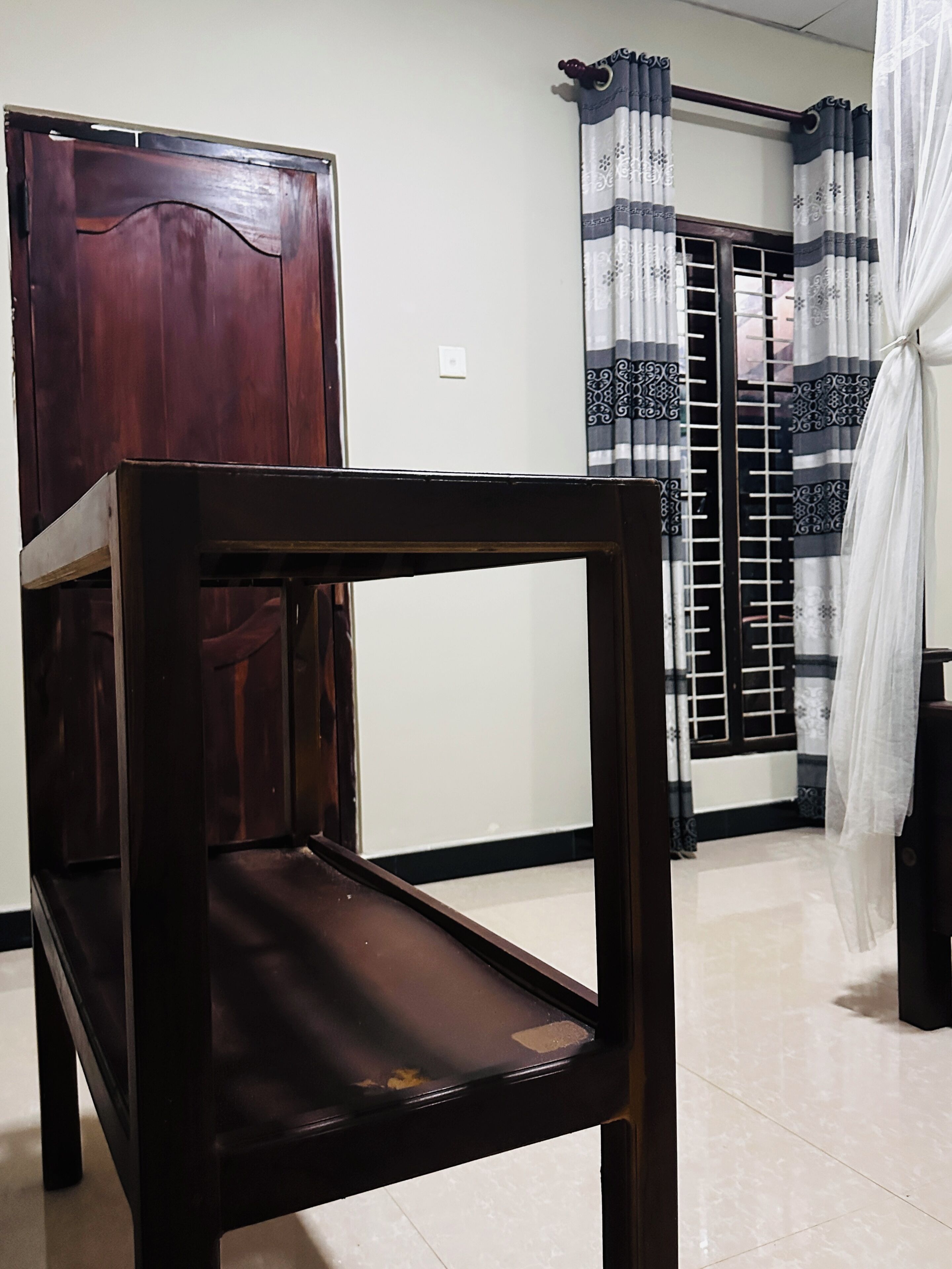 A room with a wooden chair, a wardrobe, a curtain with a pattern, and a tiled floor.