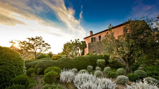 Edifici històric amb façana de pedra, envoltat d'arbres i jardins ben cuidats.