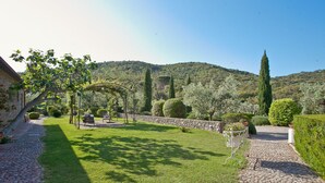 Un jardí ben cuidat amb un camí de pedra, talls de setge ordenats i una pèrgola.