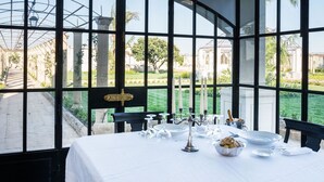 A table set for dining with a view of a garden and historical buildings.
