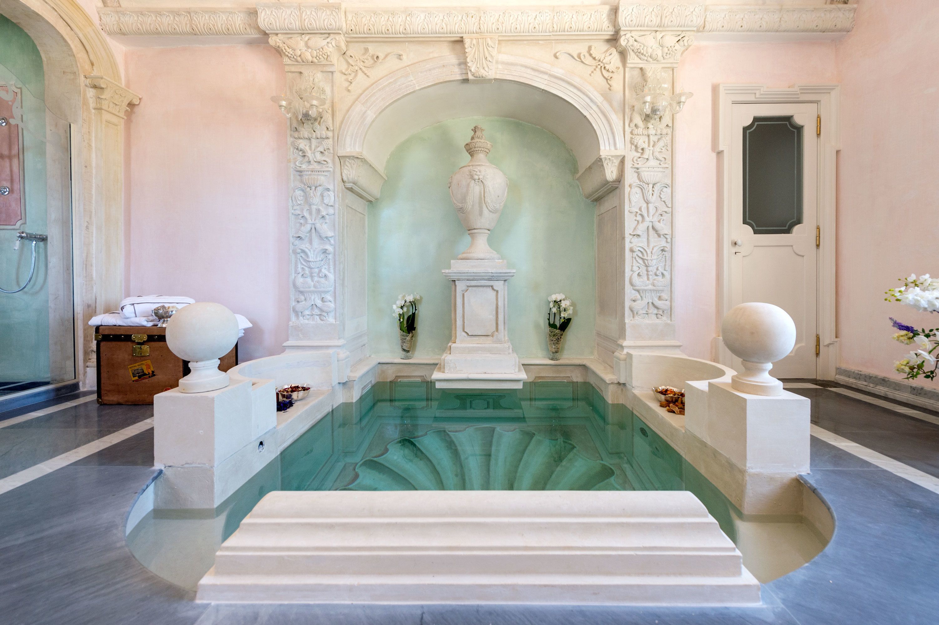 Ein luxuriöses Badezimmer mit Marmorboden, einer zentralen Fontäne und aufwendigen Wandverzierungen.