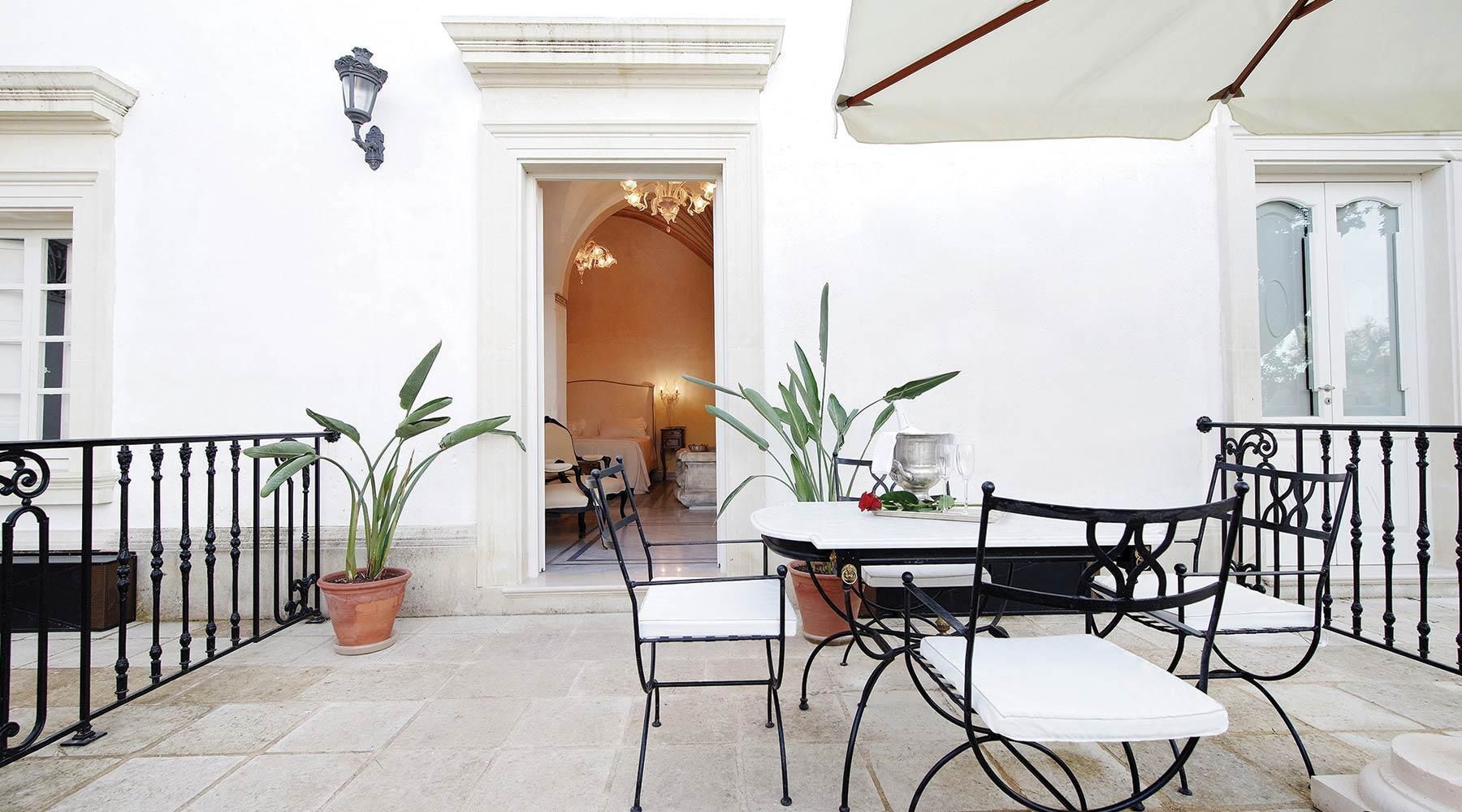 Une terrasse avec une table et des chaises, des plantes en pot et un parasol blanc.