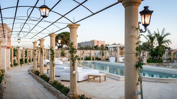 A poolside area with columns, outdoor seating, and a pergola with hanging lights.