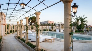 A poolside area with columns, outdoor seating, and a pergola with hanging lights. - Tenuta Mosè Charming House Relais (Alezio)