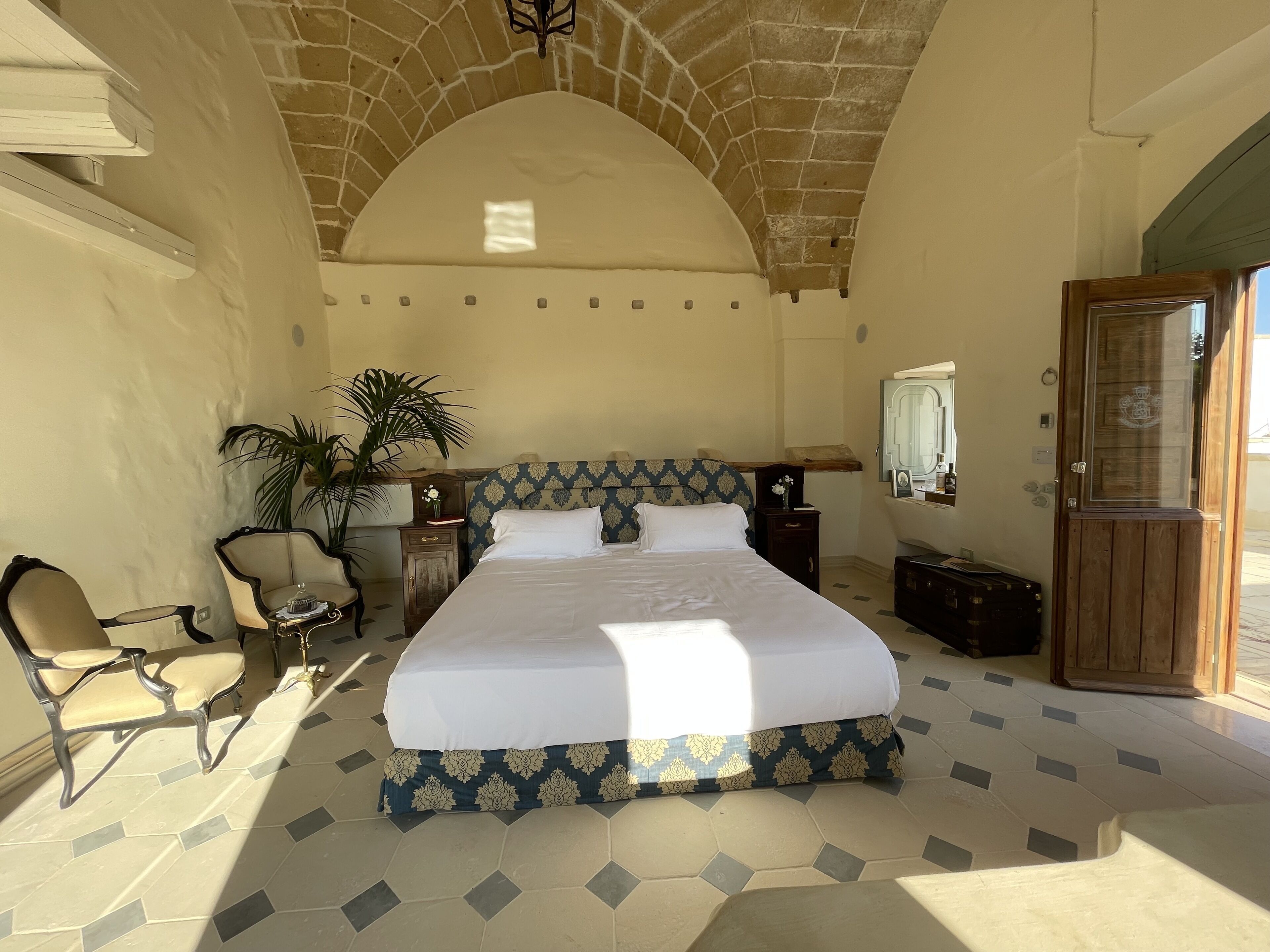 Un dormitorio espacioso con una cama grande, una silla, una mesita de noche, un espejo y una puerta.