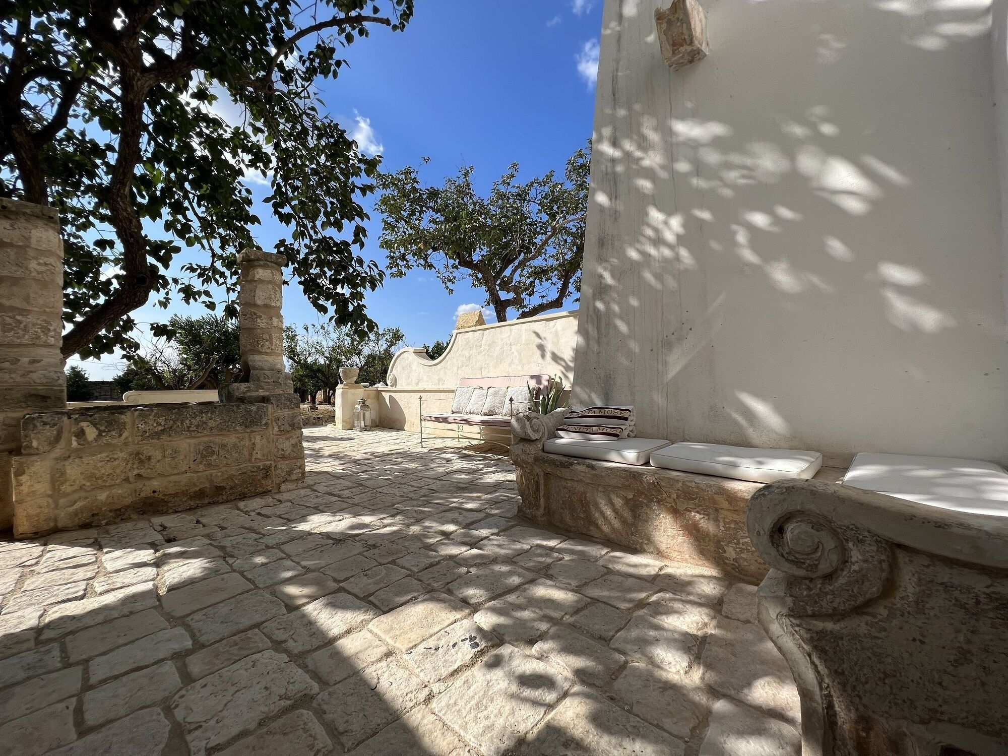 A courtyard with stone paving, a white bench, and a wall with a decorative column.