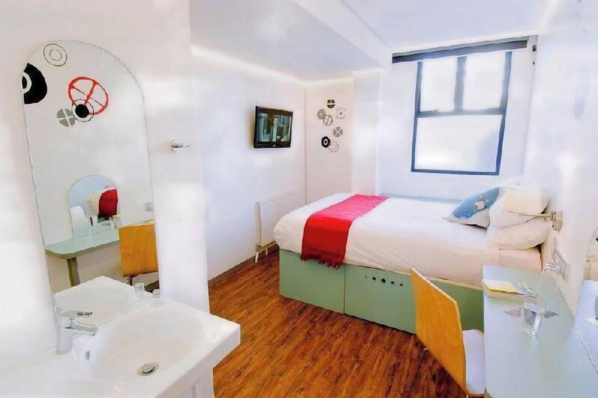 Une chambre à coucher comprenant un lit, une table de chevet, un miroir, une fenêtre et un mur agrémenté d’éléments décoratifs.