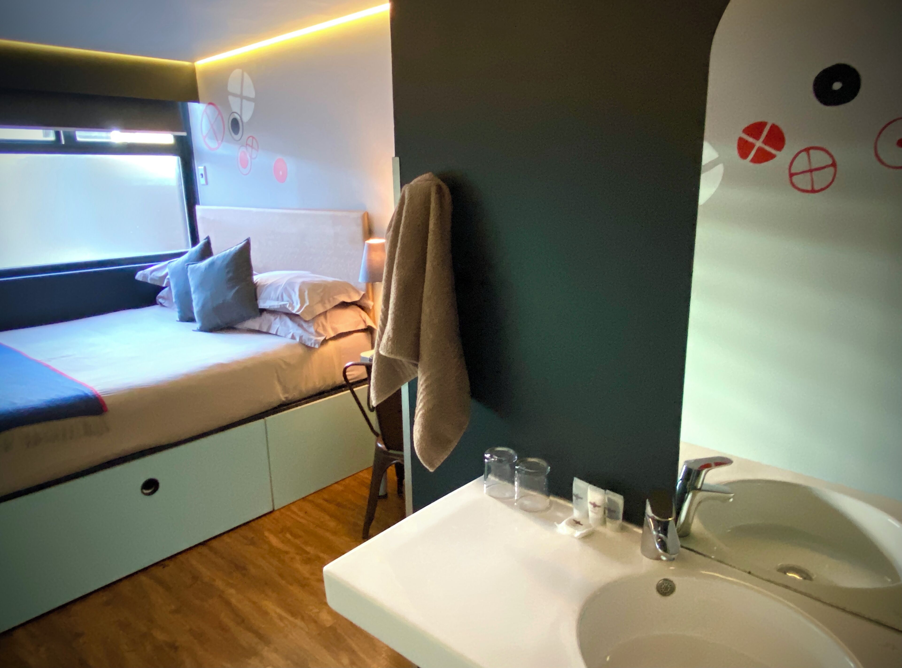 A compact bedroom with a bed, bedside table, and a small window.