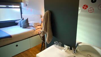 A compact bedroom with a bed, bedside table, and a small window.