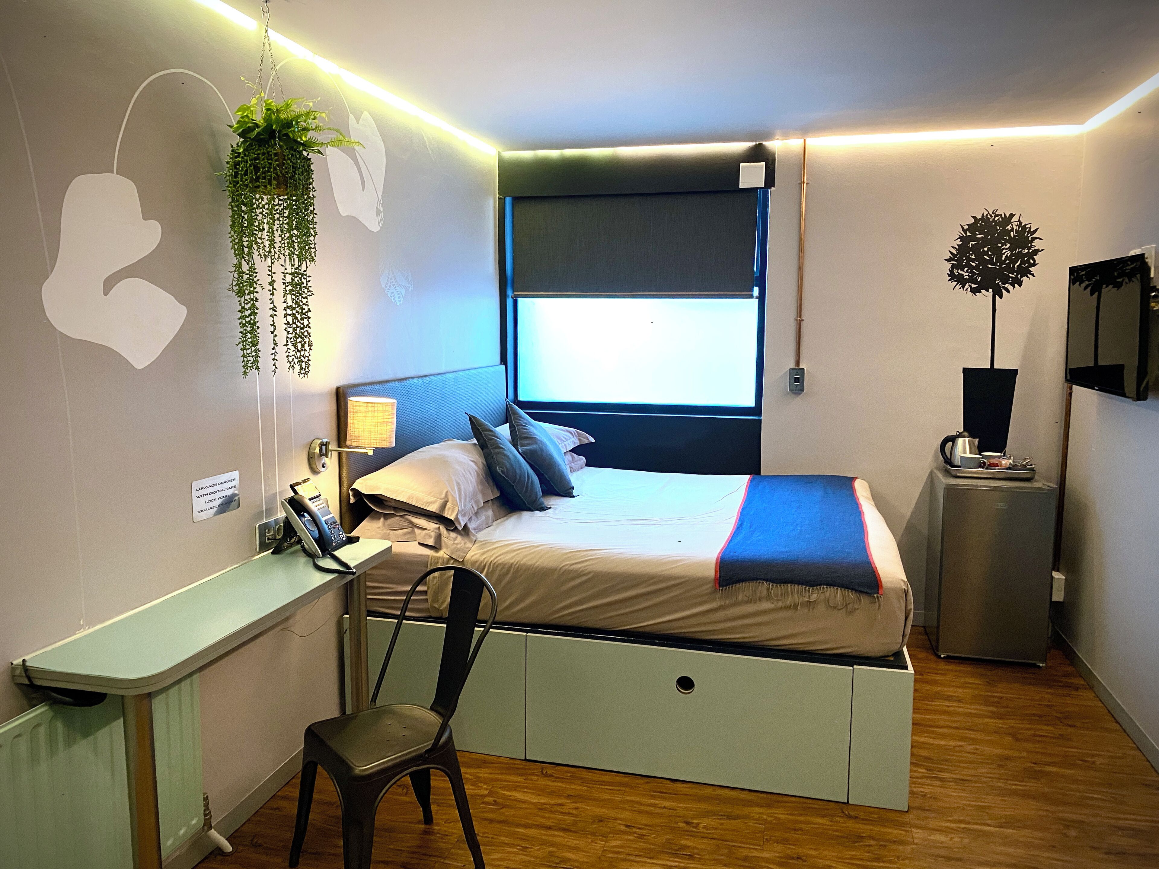 A compact bedroom with a bed, desk, chair, and a small kitchenette.