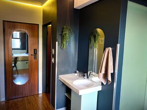 Un baño con puerta de madera, un espejo, un lavamanos y una toalla colgada en la pared.