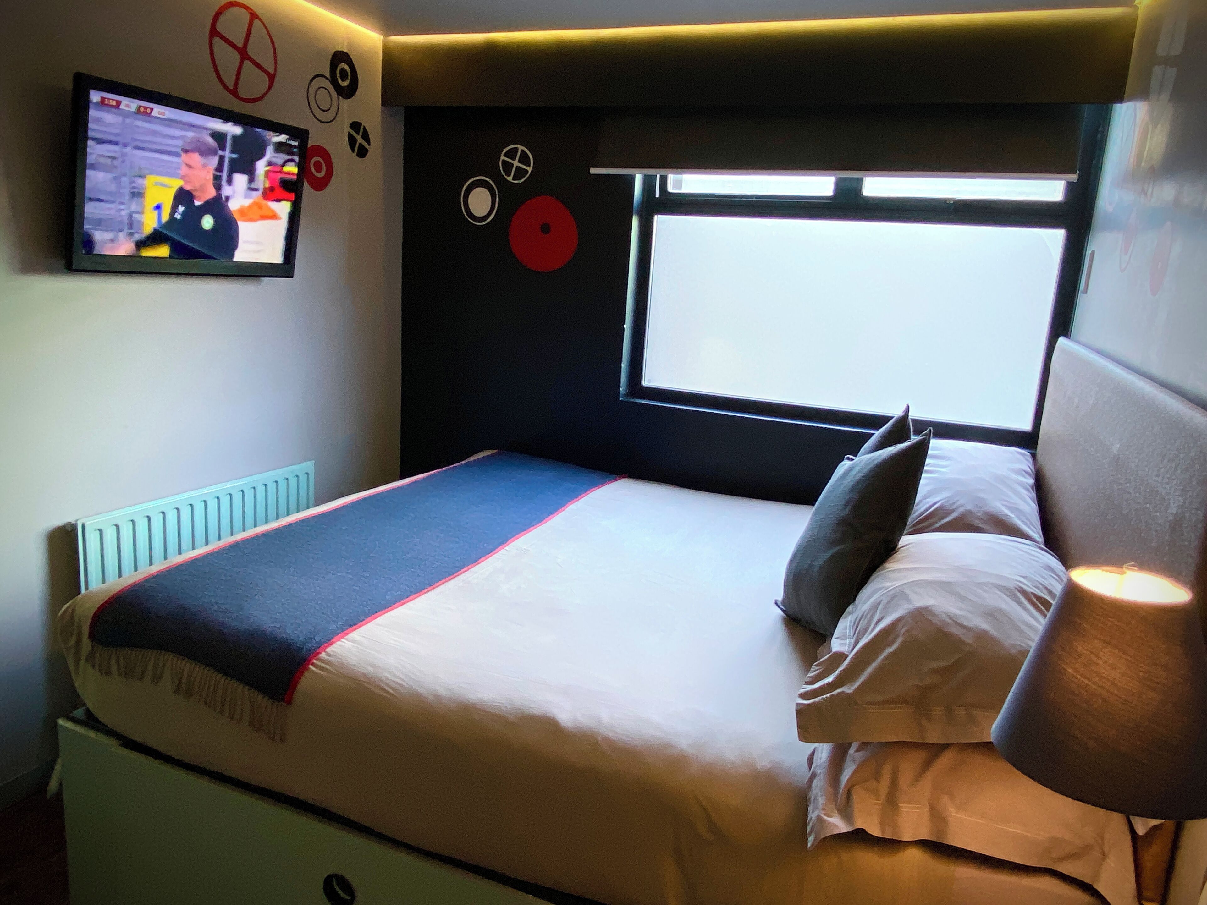 A bedroom with a bed, a window, a TV on the wall, and a radiator.