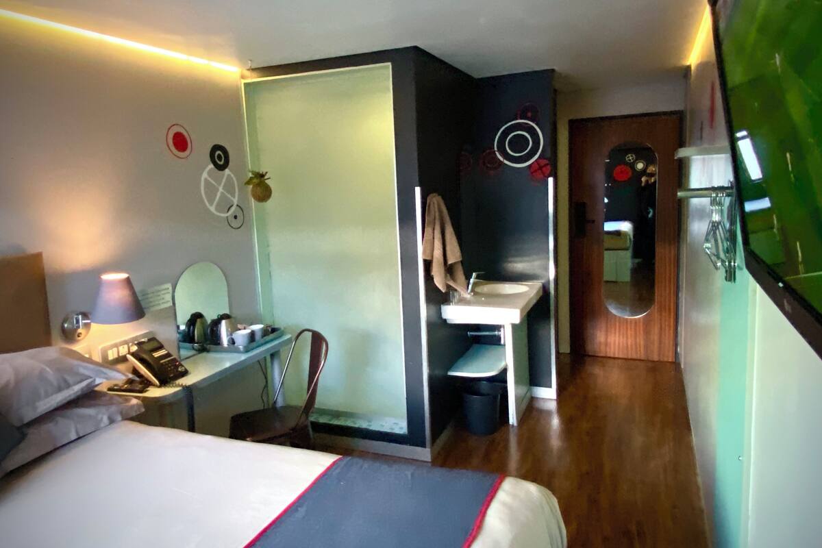 Une chambre d’hôtel comprenant un lit, un bureau avec une lampe, un miroir et une salle de bain avec un lavabo et des toilettes.