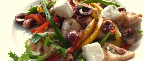 A plate of grilled chicken with vegetables and feta cheese.
