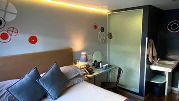 A hotel room with a bed, bedside table, lamp, mirror, and a small bathroom with a sink and mirror.