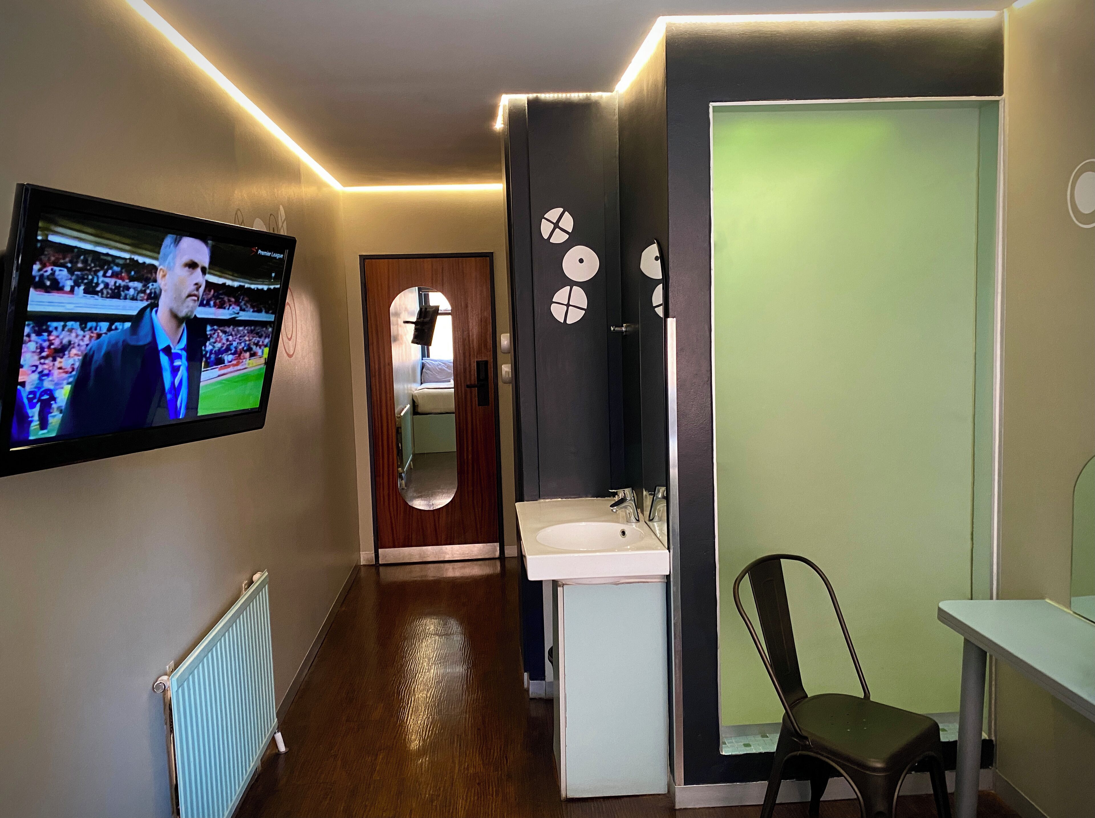 Um corredor com televisão na parede, espelho, pia e uma cadeira.
