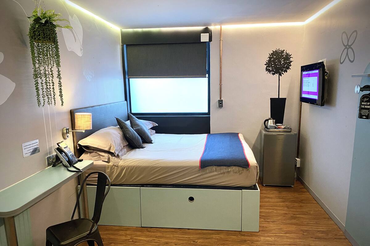 Une chambre d’hôtel moderne équipée d’un lit, d’un bureau, d’une chaise et d’une petite kitchenette.