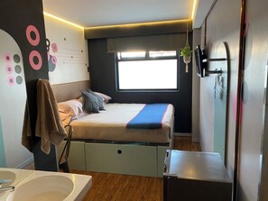 Un dormitorio moderno con cama, una planta colgante, ventana y baño con lavamanos y espejo.