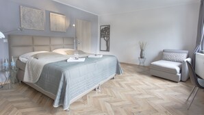 A modern bedroom with a large bed, bedside tables, a chair, and artwork on the walls. - Tm Suites (Dortmund)