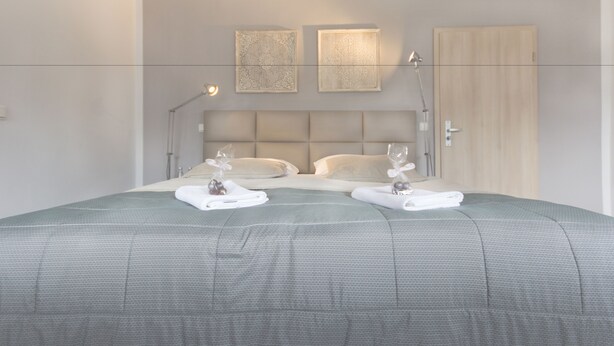 A neatly made bed with a grey bedspread, two bedside tables with lamps, and two wall-mounted light fixtures. - Tm Suites (Dortmund)