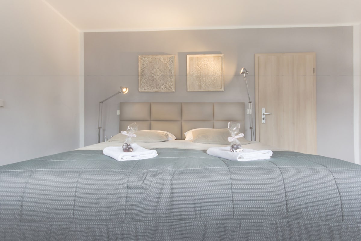 A neatly made bed with a grey bedspread, two bedside tables with lamps, and two wall-mounted light fixtures.
