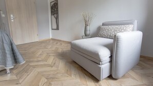 A modern bedroom with a sofa bed, a wooden door, a wall-mounted artwork, and a vase with dried plants. - Tm Suites (Dortmund)