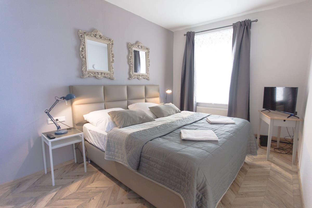 A neatly arranged bedroom with a bed, bedside tables, a TV, and two wall-mounted mirrors.