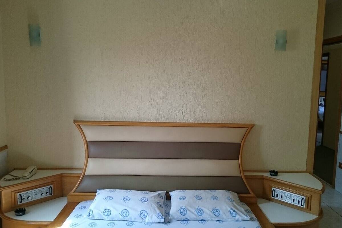 Un lit double avec une tête de lit en bois et deux tables de chevet, chacune équipée d’un téléphone et d’une prise électrique.