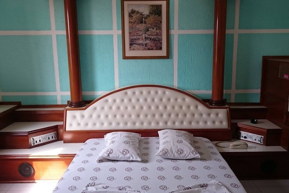 Une chambre à coucher avec une tête de lit capitonnée, deux tables de chevet, un lit avec une literie à motifs et un tableau encadré au mur.