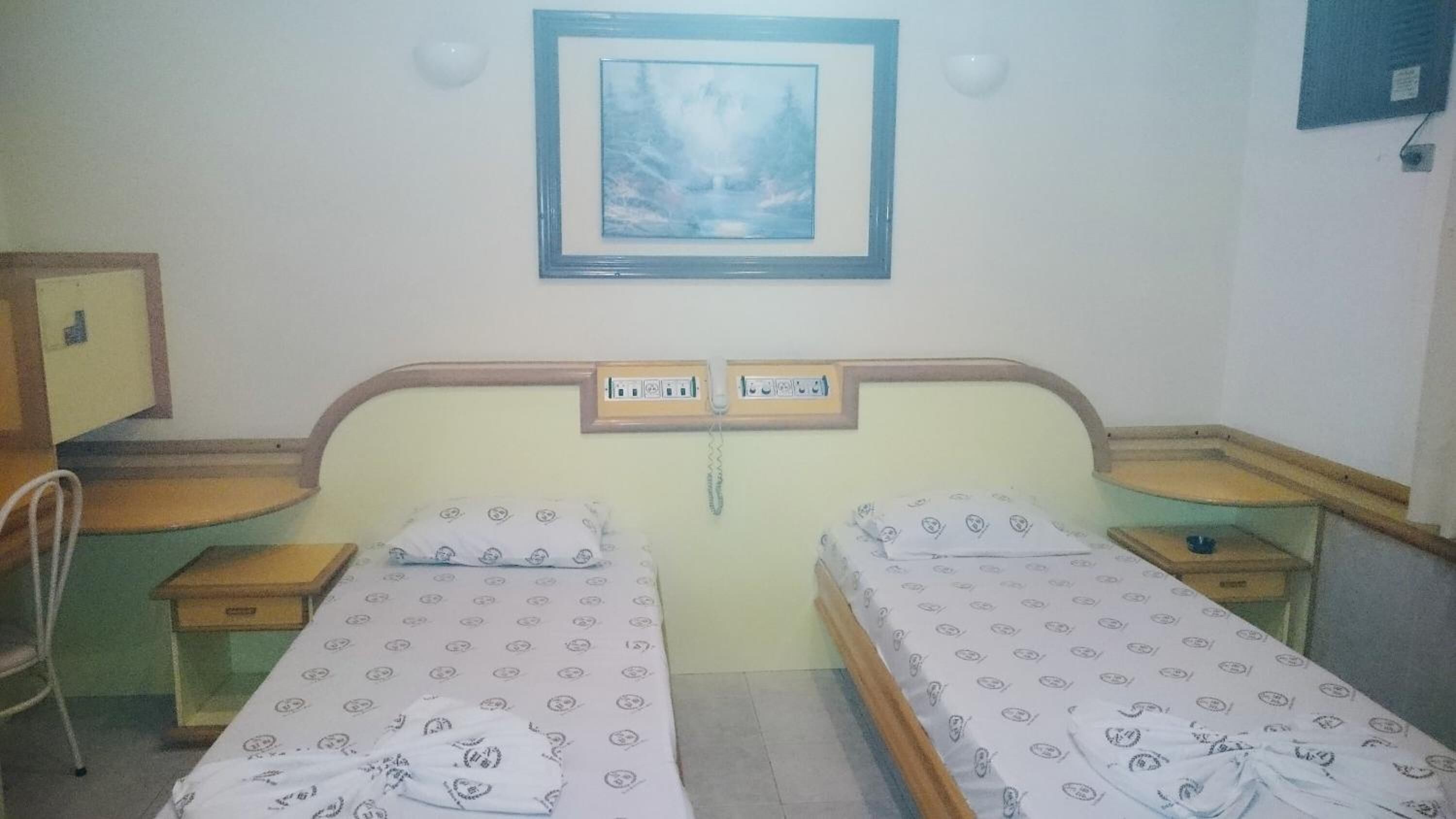 A twin room with two beds, a desk, a chair, and a painting on the wall.