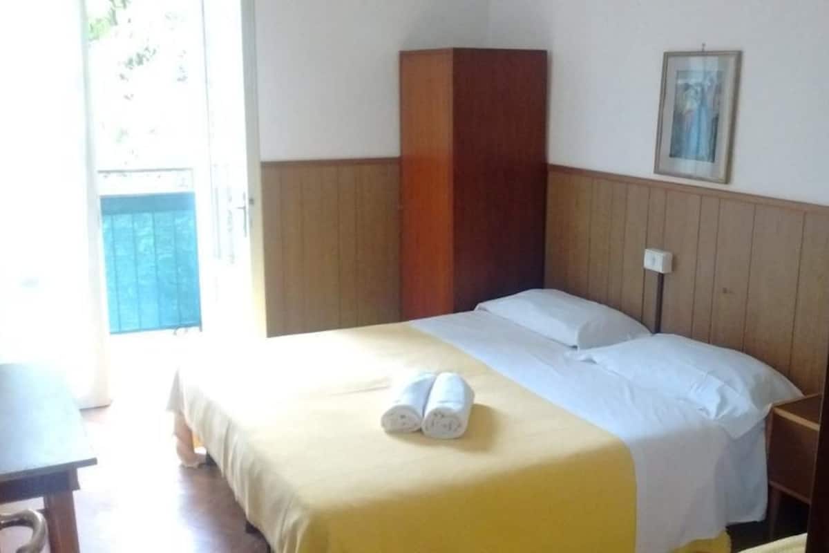 Habitació d'hotel amb un llit, un panell de capçalera de fusta, una taula de nit i una finestra.