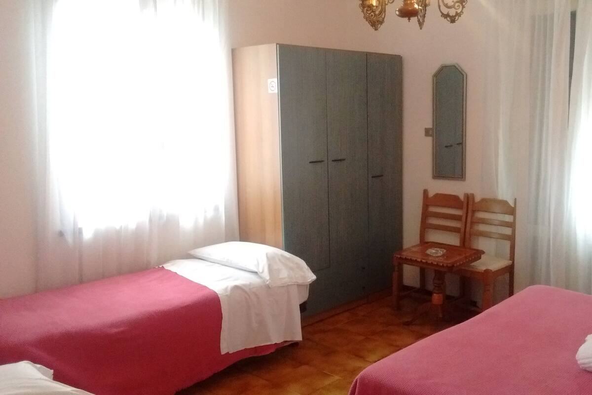 Habitació amb dos llits, una cadira de fusta, un armari i un mirall.