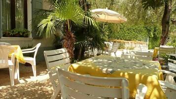 An outdoor dining area with white plastic chairs and tables, a yellow tablecloth, and a palm tree.