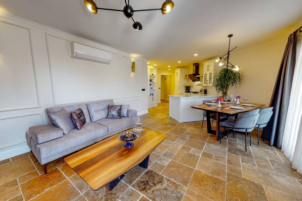 A modern living room with a grey sofa, wooden coffee table, and a dining area with a wooden table and chairs.