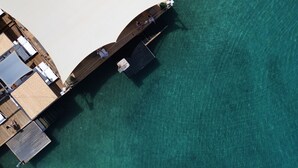 An aerial view of a resort with a wooden deck extending into clear turquoise water, a covered area with seating, and a small boat docked nearby. - Casamia Boutique Hotel (Bodrum)