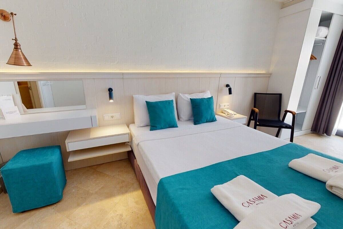 A hotel room with a bed, a desk, a chair, and a mirror.