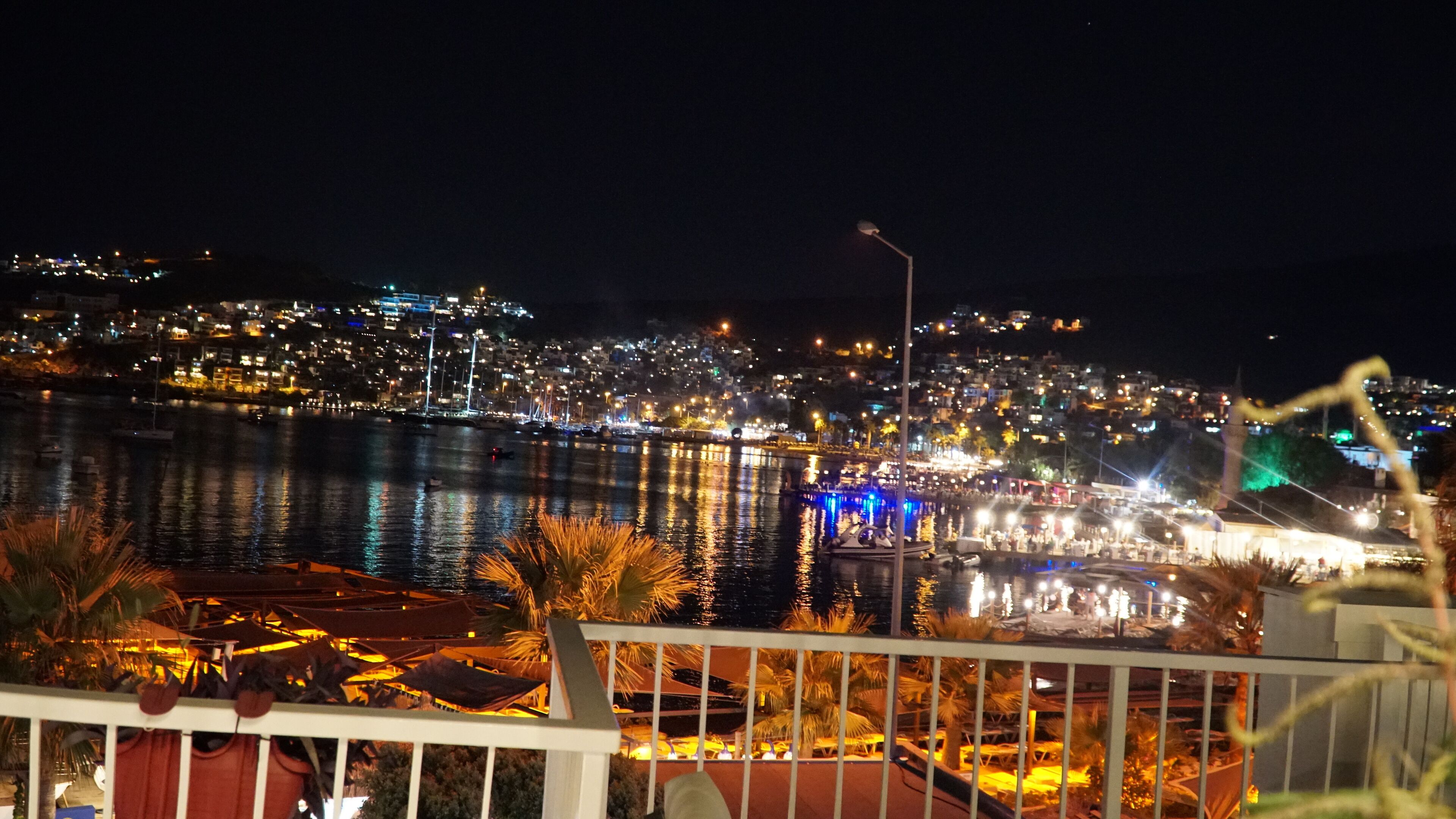 A nighttime cityscape with a waterfront, illuminated buildings, and a view of the sea.