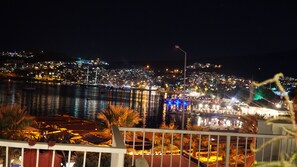 A nighttime cityscape with a waterfront, illuminated buildings, and a view of the sea.