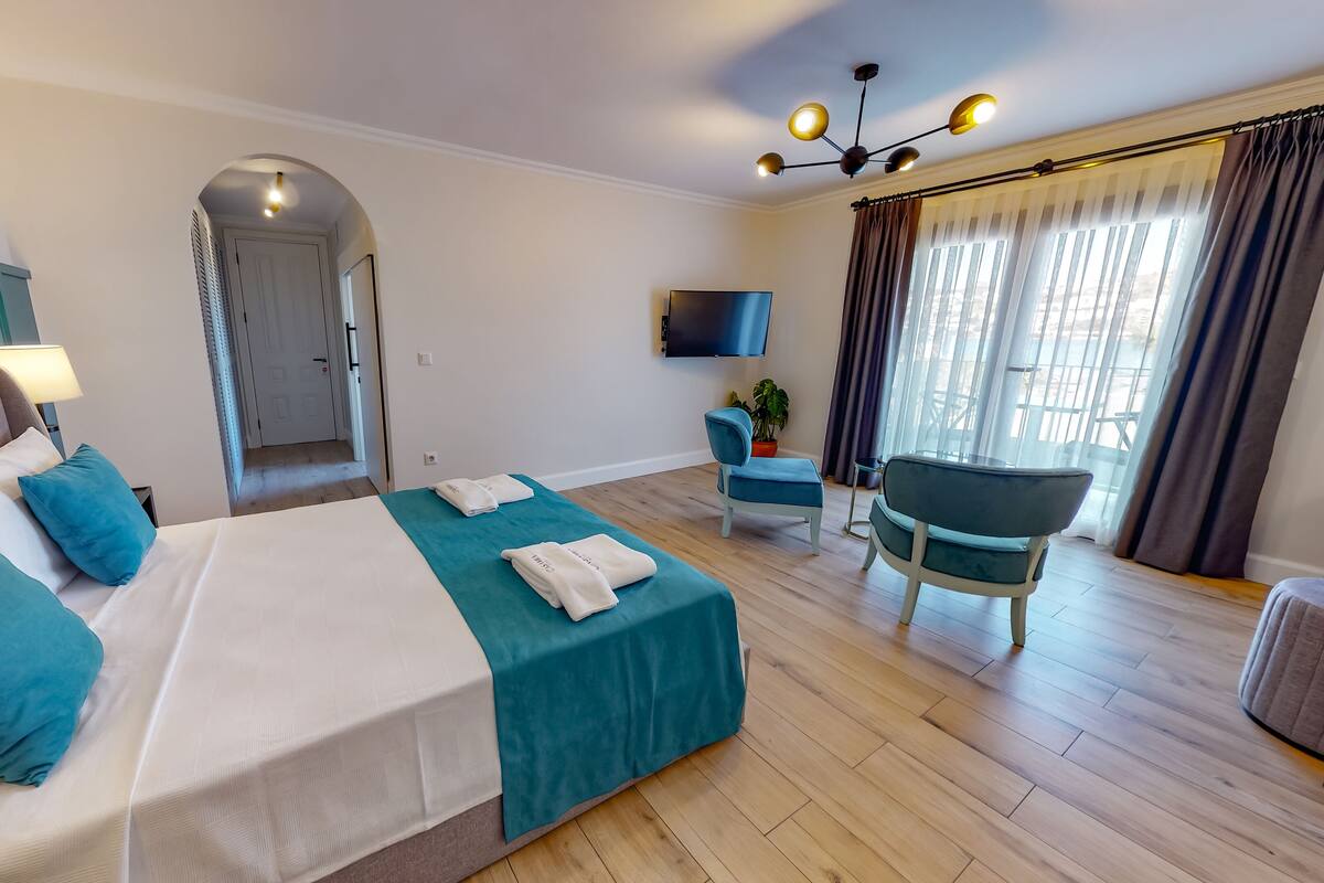 A hotel room with a bed, a desk, a chair, a TV, and a window with curtains.