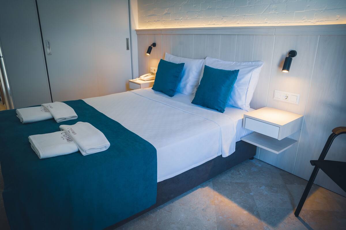 A neatly made bed with a teal bedspread and white linens, two bedside tables with lamps, and a chair.