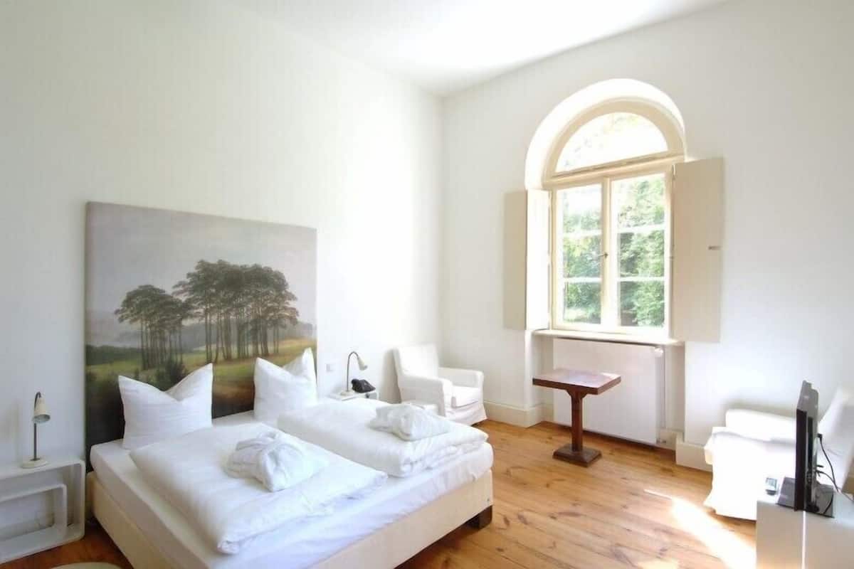 Une chambre d’hôtel avec un grand lit, un bureau, une chaise, une fenêtre à arc en plein cintre et un tableau au mur.