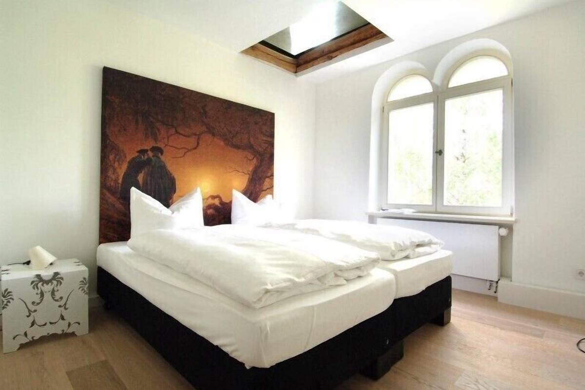 Une chambre à coucher avec un lit, un tableau au mur, une fenêtre et une table de chevet.