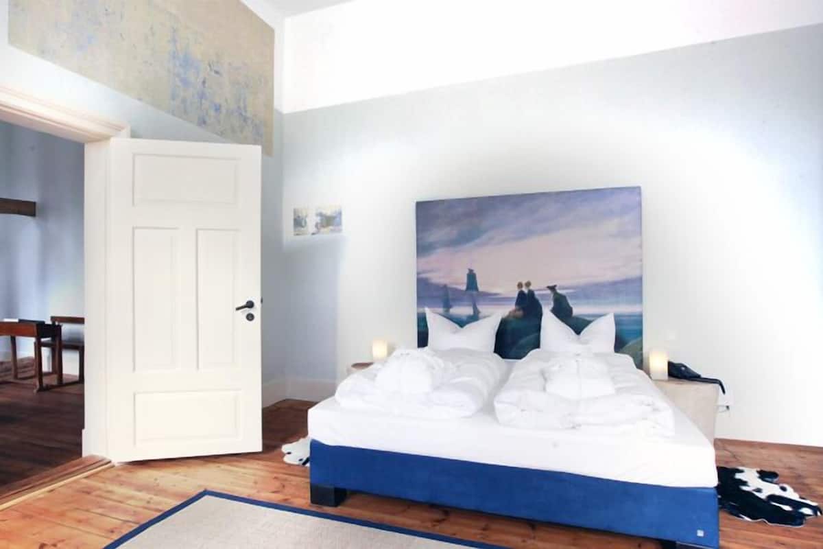 Une chambre à coucher avec un lit, un tableau et une porte qui donne sur une autre pièce.