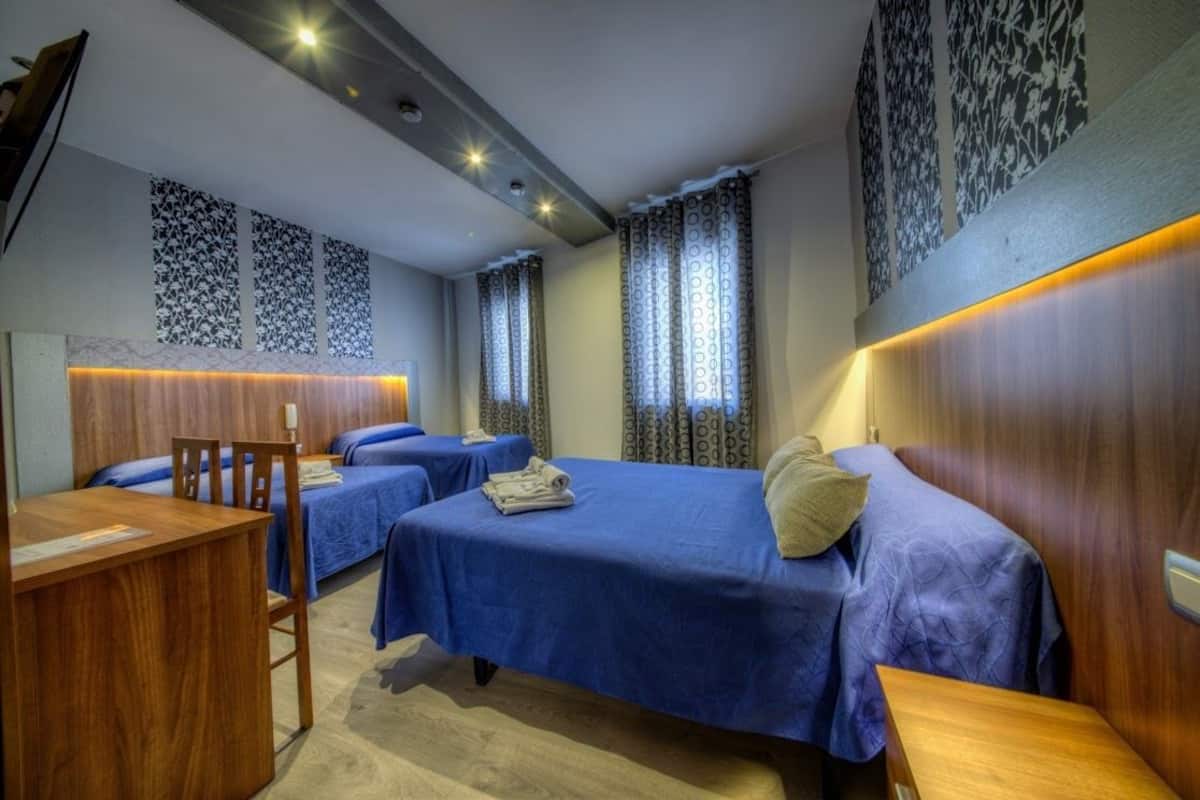 A hotel room with two beds, a wooden desk, and patterned curtains.
