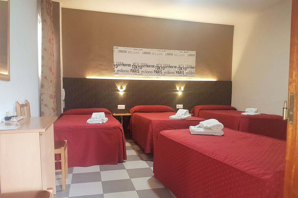 A hotel room with two single beds, a desk, a chair, and a wall-mounted sign listing various cities.