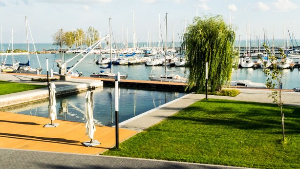 A marina with numerous boats docked, a grassy area, and a small bridge. - Alsóörs Marina Hotel (Alsoors)