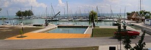 A marina with multiple boats docked, a small dock area, and a grassy area with a red boat trailer. - Alsóörs Marina Hotel (Alsoors)